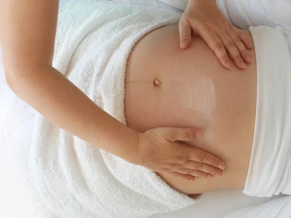 Perto das mãos femininas de um terapeuta de massagem faz uma massagem leve na barriga de uma menina grávida em uma sala de cosmetologia . — Fotografia de Stock