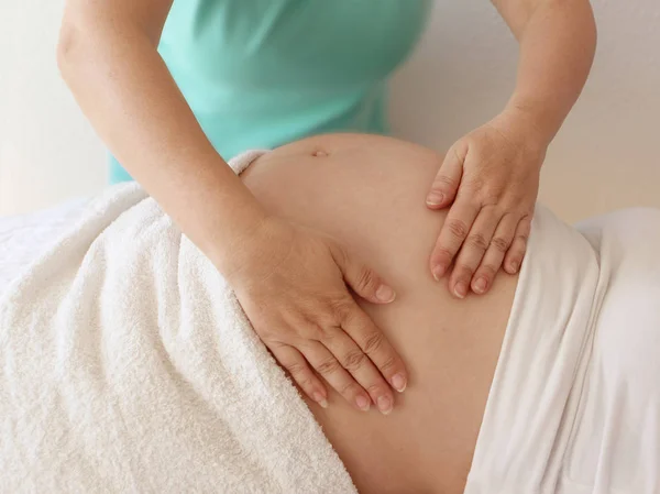 Perto das mãos femininas de um terapeuta de massagem faz uma massagem leve na barriga de uma menina grávida em uma sala de cosmetologia . — Fotografia de Stock