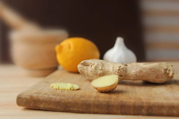 La fruta fresca de jengibre se encuentra en un fondo de madera clara junto al limón y el ajo, concepto de salud — Foto de Stock