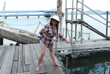 Işık Panama, ekose gömlek ve şort bir kadın ahşap bir balıkçı İskelesi üzerinde ayakta ve bir balık ağı tutan, mavi deniz