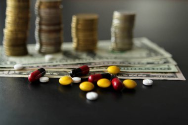 Pills ve kapsüller ve dolar banknotlar, arka planda sikke yığınları. Pahalı tedavi kavramı, sağlık yakın çekim