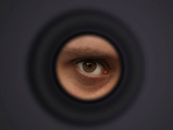 O olho de um homem olhando para fora da ocular, o conceito de vigilância, espreitando, mistério — Fotografia de Stock