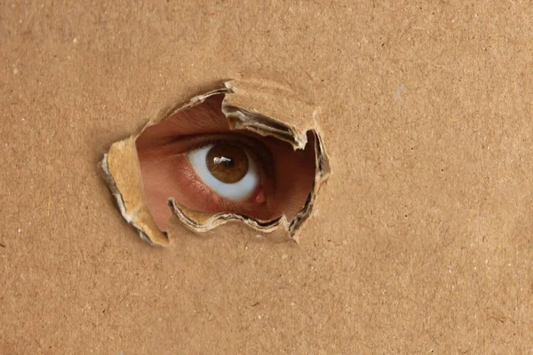 The human eye looks out of a hole in the cardboard, the concept of surveillance, peeping — Stock Photo, Image