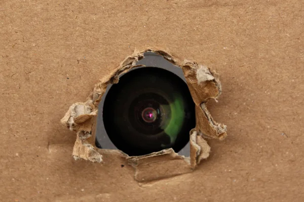Lente de câmera olha para fora do buraco no cartão, o conceito de vigilância, espreitando — Fotografia de Stock