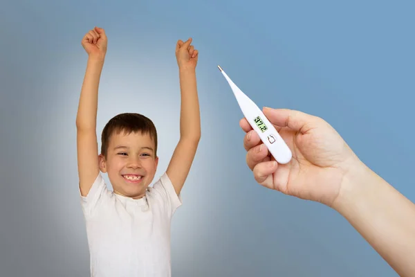 Kvinnlig hand håller vit termometer på en suddig bakgrund med en glädjefull pojke, ljus bakgrund — Stockfoto