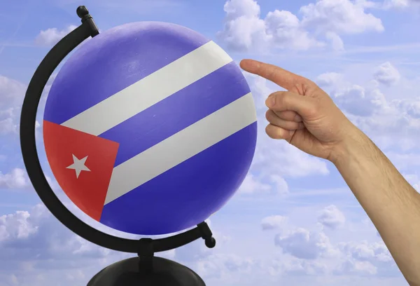 Ο δείκτης ενός αρσενικού χεριού οδηγεί σε μια υδρόγειο με μια έγχρωμη σημαία της εθνικής πολιτείας της Κούβας — Φωτογραφία Αρχείου