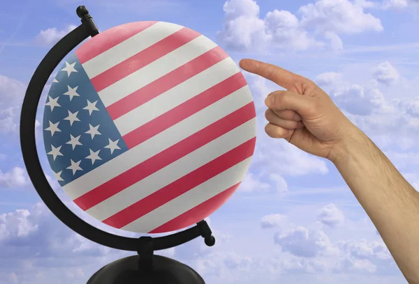 O dedo indicador de uma mão masculina aponta para um globo com uma bandeira nacional colorida Amerika — Fotografia de Stock