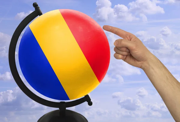 De wijsvinger van een mannelijke hand wijst naar een wereldbol met een gekleurde nationale staat vlag Roemenië — Stockfoto