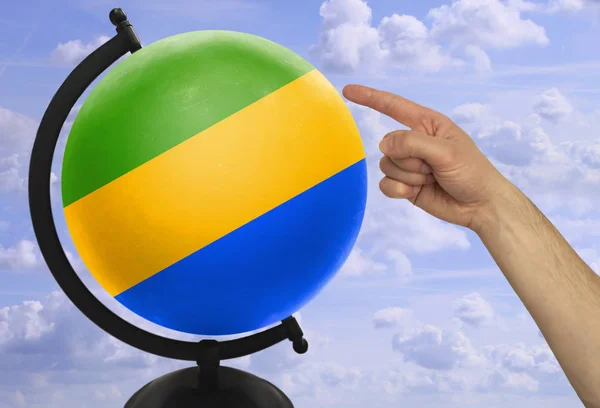 De wijsvinger van een mannelijke hand wijst naar een wereldbol met een gekleurde nationale staat vlag Gabon — Stockfoto