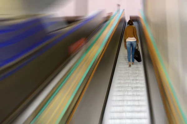the girl climbs the steps of the escalator from the underground metro against the background of blurred walls