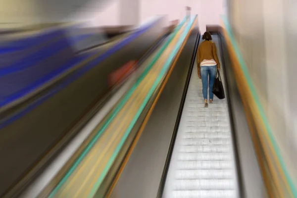 The girl climbs the steps of the escalator from the underground metro against the background of blurred walls — Stock Photo, Image