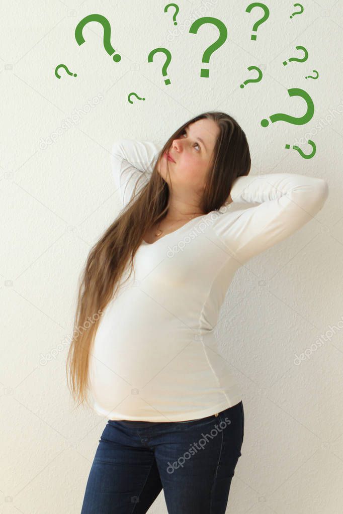 a pregnant girl in a white blouse and jeans stands with her hands behind her head and, looking up, looks up at the question marks