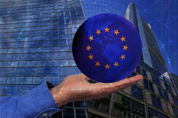Barevný modrý glóbus namalovaný v barvách vlajky Evropské unie leží na mužské ruce proti pozadí evropských mrakodrapů, symbol nových evropských a parlamentních voleb — Stock fotografie