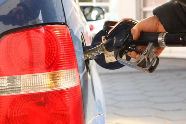 Male hand holding a refueling gun in the gas tank against the background of the car's taillights — Stock Photo, Image