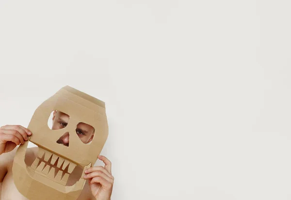 Hombre sostiene delante de la cara una máscara de cráneo hecha de cartón, lugar para el texto — Foto de Stock