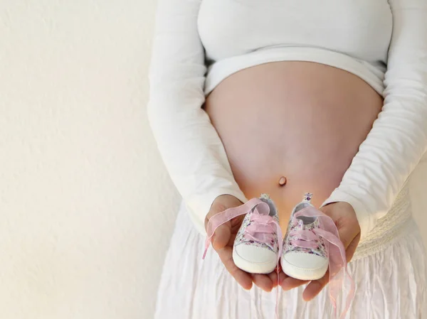 Una ragazza incinta con una grande pancia sta tenendo piccole scarpe rosa davanti alla sua pancia — Foto Stock