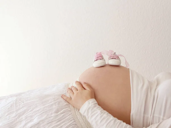 Pantofi roz mici sunt pe burta rotundă a unei femei însărcinate — Fotografie, imagine de stoc