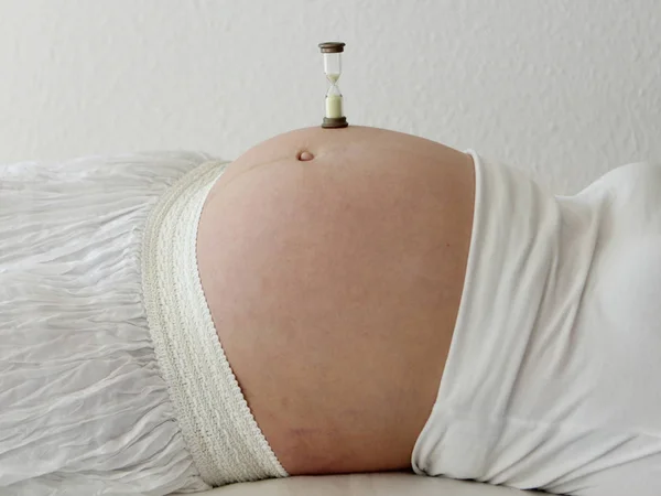 Clepsidră stand pe burta rotundă a unei femei însărcinate — Fotografie, imagine de stoc