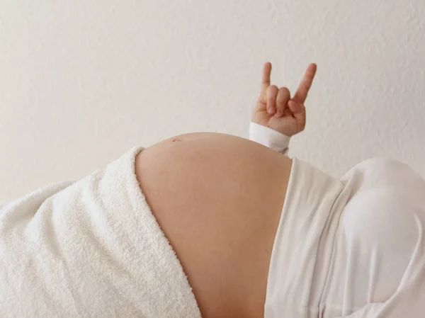 Fată însărcinată cu o burtă mare goală în haine albe se află cu o mână ridicată într-o victorie pozitivă a gestului, aproape — Fotografie, imagine de stoc