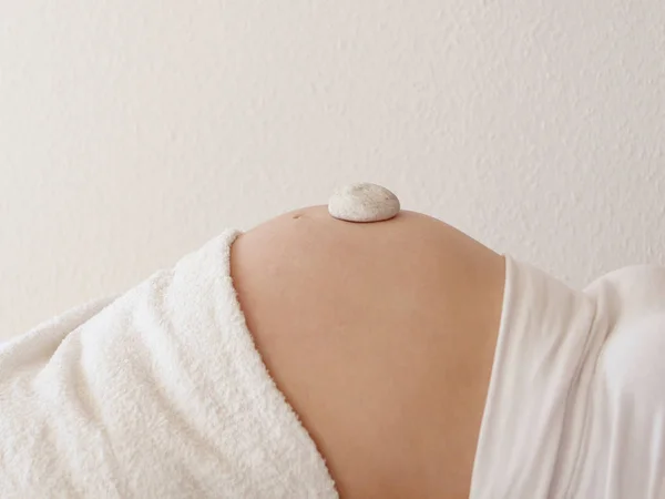 Ragazza incinta con una pietra rotonda bianca su una grande pancia nuda in vestiti bianchi si trova, primo piano — Foto Stock