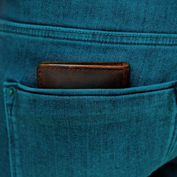 Brązowy męski portfel z wysokiej jakości prawdziwej skóry leży w tylnej kieszeni niebieskie dżinsy męskie, stonowanych w kolorze turkusowym zdjęcie, kwadrat — Zdjęcie stockowe