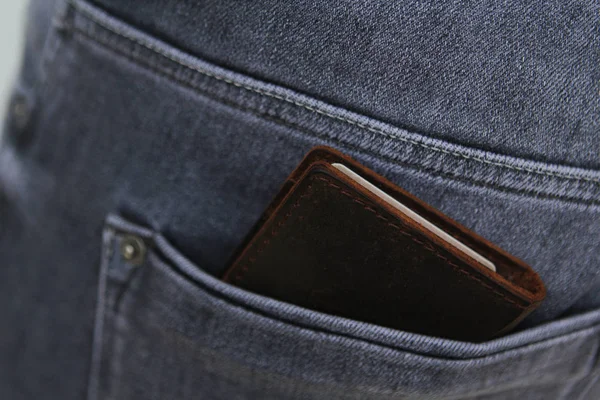 Donkere heren portemonnee gemaakt van hoogwaardig echt leer ligt in de achterzak van grijze jeans voor heren — Stockfoto