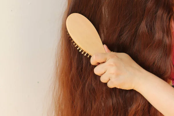 Menina com longos cabelos vermelhos escuros penteando-os com um pente de madeira, horizontal, close-up — Fotografia de Stock