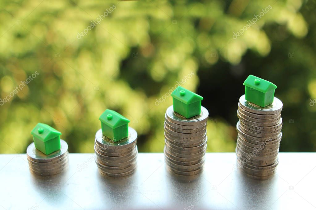 models of houses are located on stacked stacks of coins on a growing on the table on a blurred green natural background, the concept of money growth
