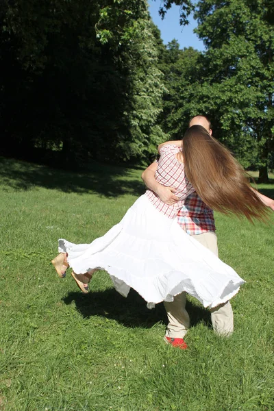 Hombre rodeando a una mujer en un vestido largo con el pelo largo en el parque, vista trasera — Foto de Stock