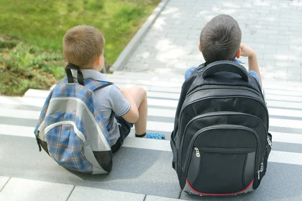 Δύο μαθητές, φίλοι, αδέλφια με σχολικές τσάντες κάθονται στα σκαλιά του σχολείου, επιστροφή στο σχολείο έννοια — Φωτογραφία Αρχείου