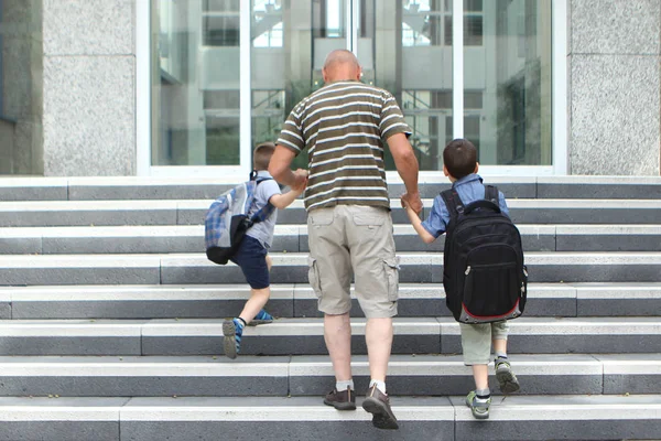 Homem idoso leva dois netos com sacos escolares, de mãos dadas, subir as escadas, De volta ao conceito de escola — Fotografia de Stock