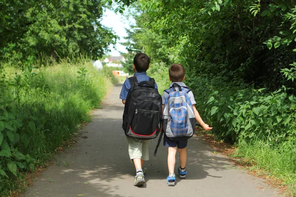 Δύο αγόρια, αδέλφια με σχολικές τσάντες πάνε στο σχολείο στην πίστα, επιστροφή στο σχολείο έννοια — Φωτογραφία Αρχείου