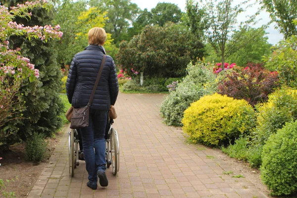 Женщина в черном пиджаке несет пожилую женщину-инвалида в инвалидном кресле — стоковое фото