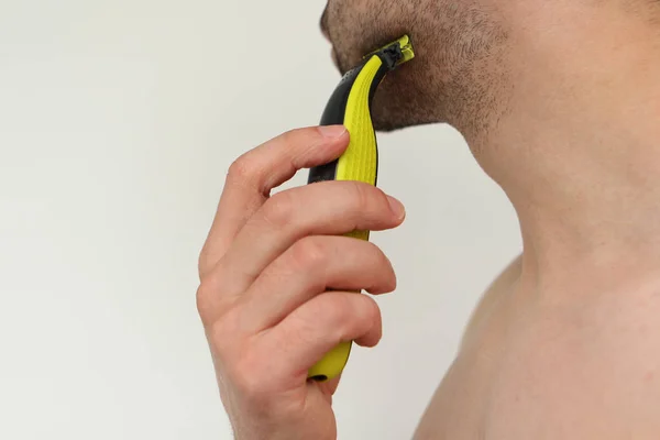 Young man with a two-day dark stubble shaves with an electric razor — Stock Photo, Image