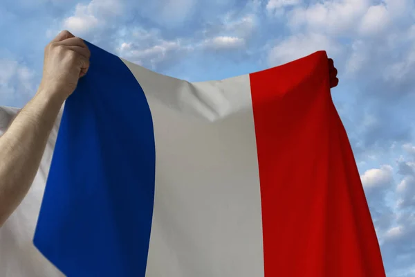 Beautiful national flag of the country of france in male hands against the blue sky with clouds — Stock Photo, Image