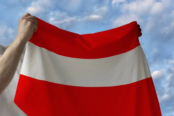 Prachtige nationale vlag van het land van Oostenrijk in mannelijke handen tegen de blauwe hemel met wolken — Stockfoto