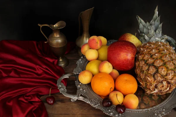 Красивый натюрморт со свежими фруктами и шелковой тканью с мягкими складками на серебряном блюде, медные кувшины, концепция изысканной роскоши — стоковое фото