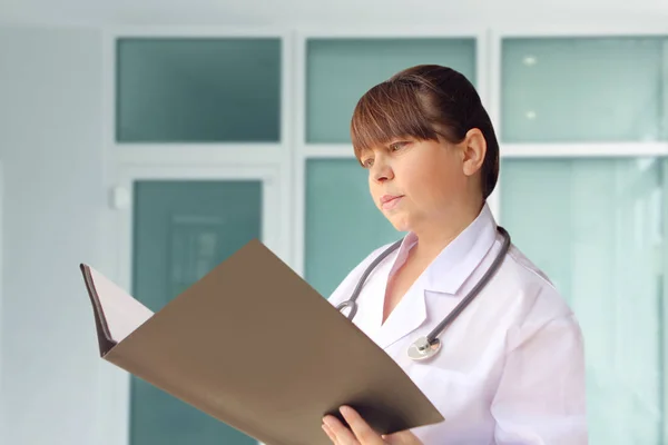 Жінка-лікар у білому пальто з фонендоскопом на шиї, що тримає папку з документами в лікарні — стокове фото
