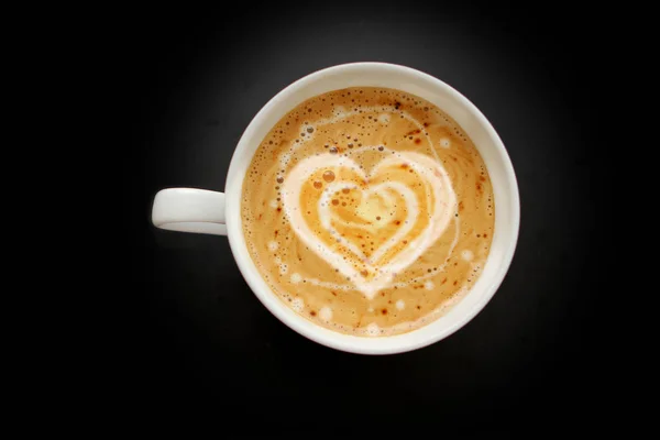 Taza de café blanco ancho con crema en forma de corazón, capuchino sobre un fondo negro con viñeta, vista superior, ahorrar espacio, primer plano, concepto de amor — Foto de Stock