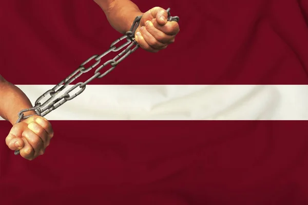 men\'s hands chained in heavy iron chains against the background of the flag of Latvia on a gentle silk with folds in the wind, the concept of the movement in support of human rights