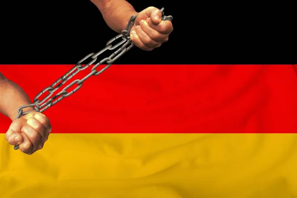 Męskie ręce przykuty w ciężkich łańcuchach żelaza na tle flagi Niemiec na delikatnym jedwabiu z fałdami na wietrze, pojęcie ruchu na rzecz praw człowieka — Zdjęcie stockowe