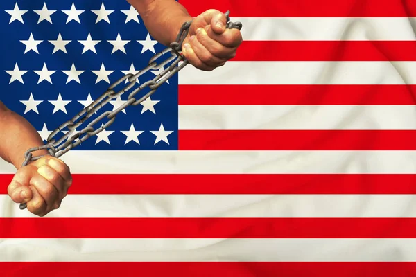 Mãos de homens acorrentados em cadeias de ferro pesado contra o fundo da bandeira da América em uma seda suave com dobras no vento, o conceito do movimento em apoio dos direitos humanos — Fotografia de Stock