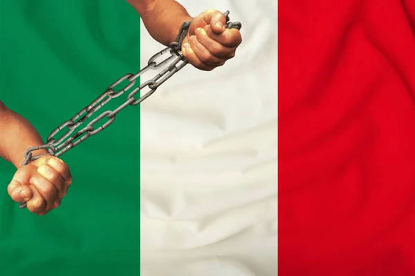 Male hands chained in heavy iron chains against the background of the flag of Italy on a gentle silk with folds in the wind, the concept of the human rights movement — Stock Photo, Image