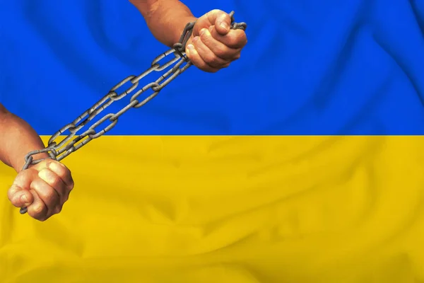 Mužských rukou spoutaných těžkými železnými řetězy proti pozadí vlajky Ukrajiny na mírném hedvábí s záhyby ve větru, pojetí hnutí na podporu lidských práv — Stock fotografie