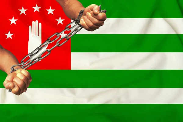 male hands chained in heavy iron chains against the background of the flag of the State of Abkhazia on silk, the concept of the movement in support of human rights