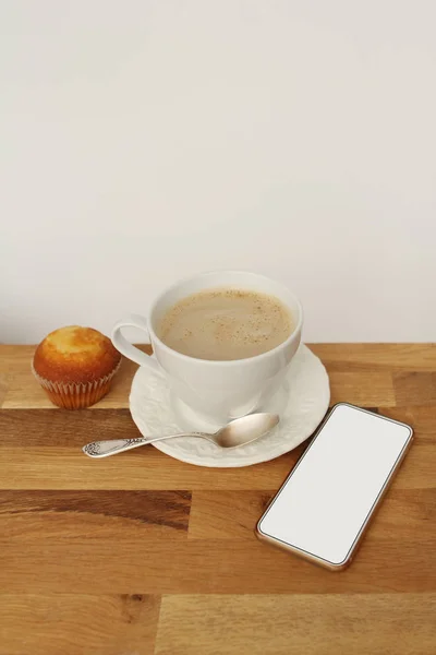 나무 테이블에 빈 흰색 화면, 커피 와 컵 케이크와 흰색 휴대 전화의 이미지를 조롱 — 스톡 사진