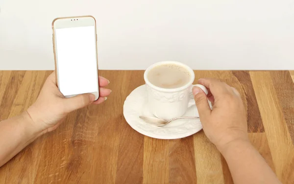 Attrappe Bild weiblicher Hände mit weißem Handy mit leerem weißen Bildschirm und Tasse Kaffee — Stockfoto