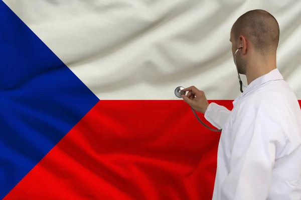 Doctor masculino en bata blanca aplicado un instrumento médico con un estetoscopio a la bandera nacional, vista posterior, concepto, espacio de copia — Foto de Stock