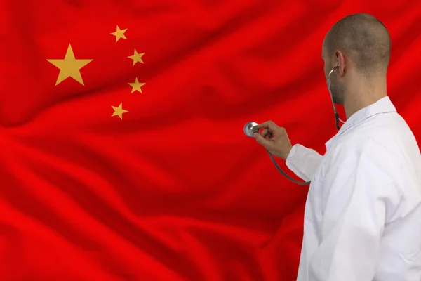 male doctor in white coat applied a medical instrument with a stethoscope to the national flag China, back view, concept, copy space