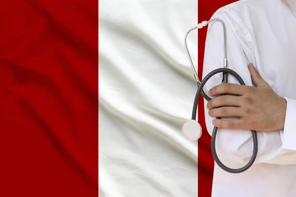 Doctor masculino con bata blanca sosteniendo en su mano un instrumento médico con un estetoscopio en el fondo de la bandera nacional Perú, primer plano, concepto, espacio de copia — Foto de Stock